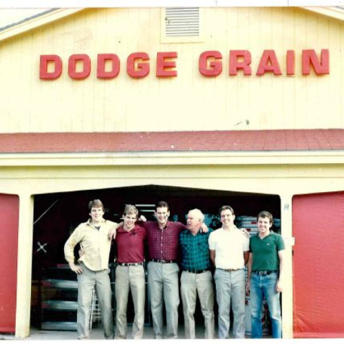 A group of seven men standing in front of a building with the sign 