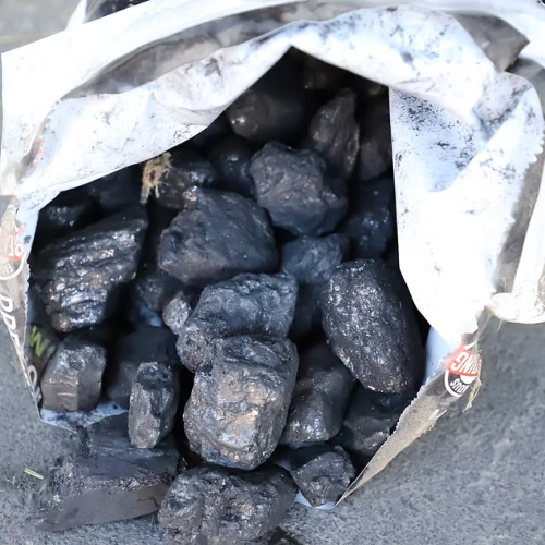 Open bag of coal chunks spilling onto a gray surface. The coal is shiny and dark, suggesting a rustic, industrial tone.