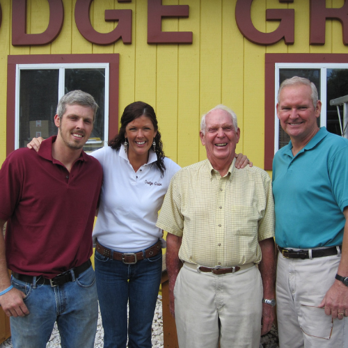 Four people smiling in front of a colorful building with a sign that reads 