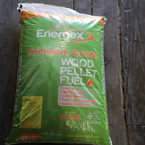 A 40-pound bag of EnergeX Premium Grade Wood Pellet Fuel on a wooden floor. The green packaging highlights features like low ash, high BTU, and carbon neutrality.